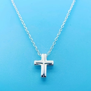 Puede incluir: Un collar de cadena de plata con un pequeño colgante de cruz de plata.