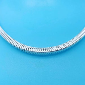 May include: A silver snake chain necklace on a blue background.