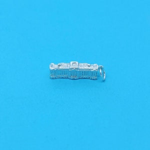 May include: Silver charm in the shape of a building with a detailed facade. The charm has a loop for attaching to a bracelet or necklace.