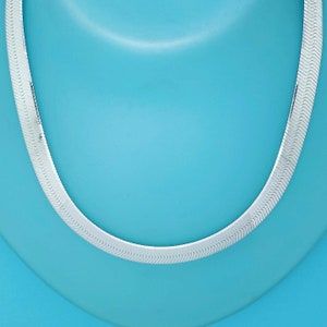 May include: A silver chain necklace with a classic, flat, snake chain design. The chain is on a light blue background.