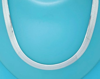 Puede incluir: Un collar de cadena de plata con un diseño clásico de cadena de serpiente plana. La cadena está sobre un fondo azul claro.