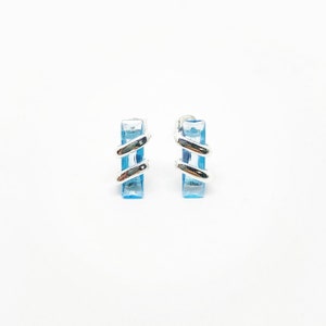 May include: A pair of silver earrings with blue topaz stones. The stones are rectangular and have a silver band around them.