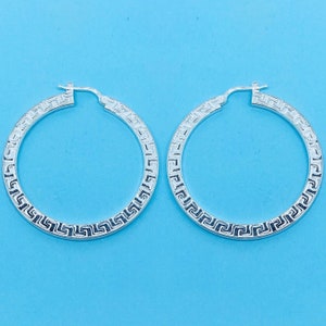 May include: A pair of silver hoop earrings with a geometric pattern around the edge.