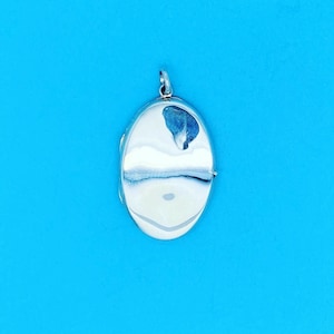 May include: A silver oval locket with a smooth, reflective surface. The locket has a simple design and is perfect for holding a small photo or memento.