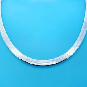 May include: A silver snake chain necklace on a blue background.