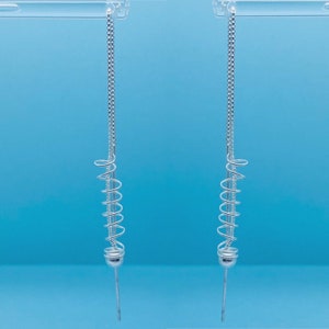 May include: A pair of silver dangle earrings with a spiral design and a small ball at the bottom.