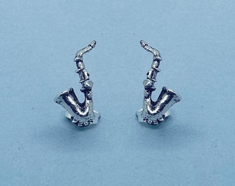 May include: A pair of silver saxophone earrings. The earrings are small and detailed, with the saxophone's bell facing forward.
