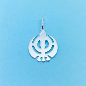 Op de afbeelding: Een zilveren hanger met het Khanda-symbool, een belangrijk symbool in het Sikhisme. De hanger heeft een cirkelvormig ontwerp met een centraal tweesnijdend zwaard, geflankeerd door twee gebogen zwaarden en een cirkel. Het hangt aan een kleine lus.