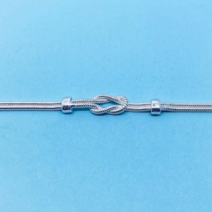 May include: A silver chain bracelet with a knot design. The chain is made of small, linked circles.