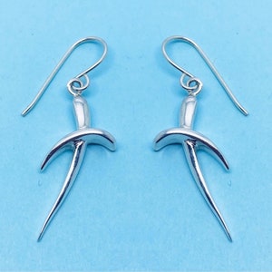May include: A pair of silver earrings featuring a distinctive, abstract design. The earrings are shaped like a stylised bird with a long, pointed tail.
