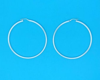 May include: A pair of silver hoop earrings on a blue background.