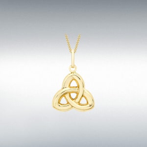 Puede incluir: Un collar con colgante dorado con un diseño de nudo celta. El colgante, un diseño entrelazado de tres partes, cuelga de una fina cadena dorada. El collar se muestra sobre un fondo gris degradado.