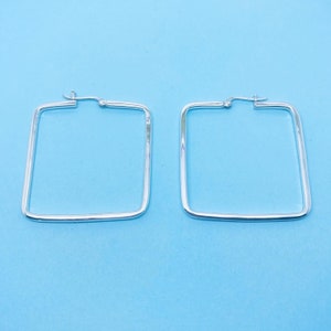 May include: A pair of silver square hoop earrings. The earrings are simple and elegant.