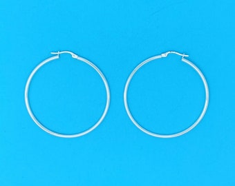 May include: A pair of silver hoop earrings on a blue background.