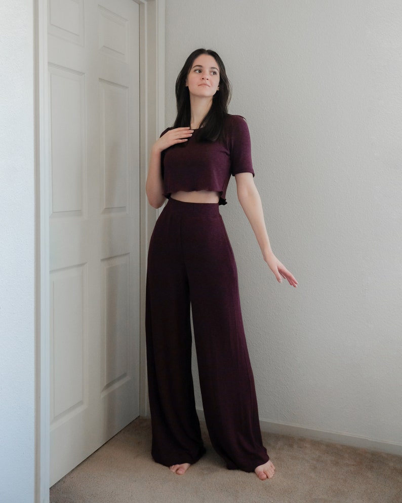 Op de afbeelding: Een tweedelige bordeauxrode outfit met een cropped top met korte mouwen en een broek met wijde pijpen. De top heeft een licht gerimpelde zoom. De outfit is gemaakt van een zachte, getextureerde stof. De broek heeft een hoge taille en een vloeiend silhouet.
