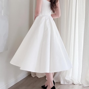 May include: A white, sleeveless dress with a fitted bodice and a flared skirt. The dress is knee-length and paired with black high-heeled shoes. The dress has a classic, elegant design, suitable for formal events.