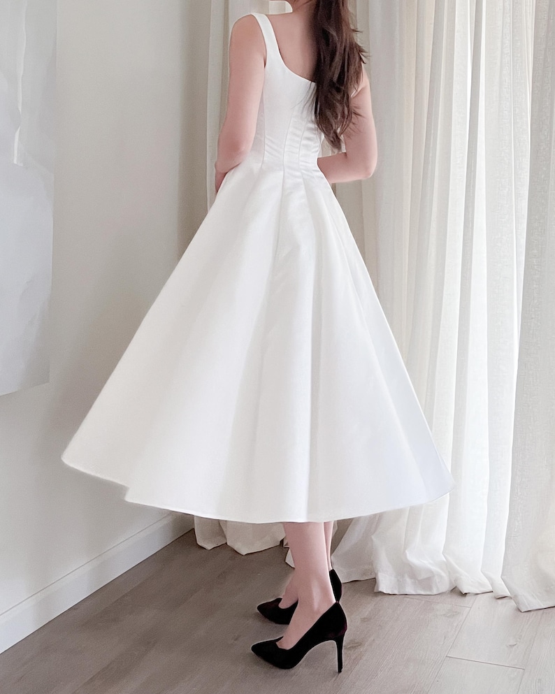 May include: A white, sleeveless dress with a fitted bodice and a flared skirt. The dress is knee-length and paired with black high-heeled shoes. The dress has a classic, elegant design, suitable for formal events.