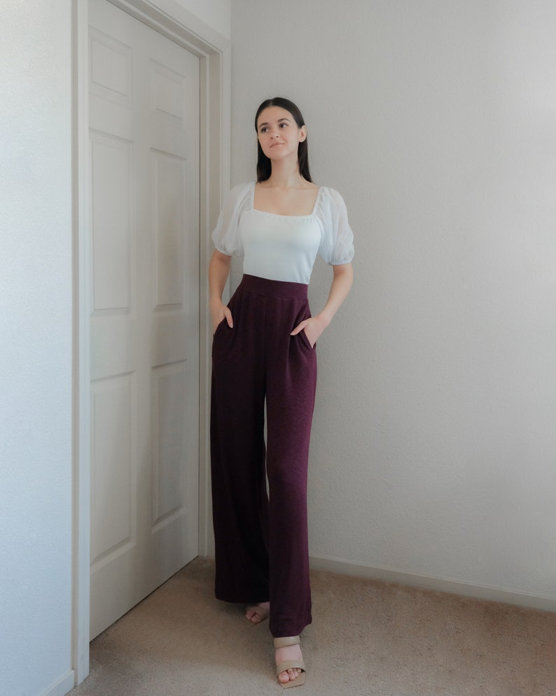Op de afbeelding: Een witte top met een vierkante halslijn en korte, doorschijnende mouwen, gecombineerd met een wijde, bordeauxrode broek. De broek heeft zakken. De outfit wordt afgemaakt met beige sandalen. Het model staat bij een witte deur en muur.