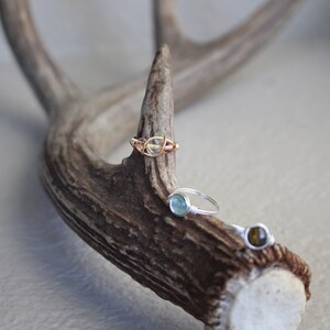 May include: Three wire-wrapped rings with different colored gemstones. The rings are displayed on a piece of antler.