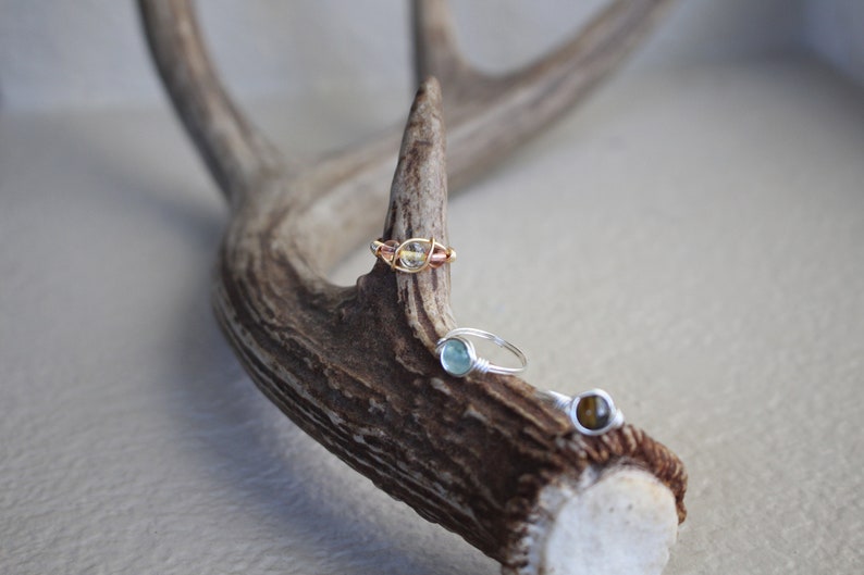 May include: Three wire-wrapped rings with different colored gemstones. The rings are displayed on a piece of antler.