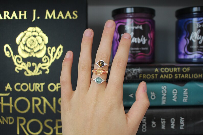May include: Three silver rings with different colored gemstones. The rings are stacked on a finger. The gemstones are a tiger's eye, a carnelian, and an aquamarine.