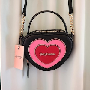 May include: Black heart-shaped crossbody bag with a pink and red heart design. The bag has a gold chain strap and a top handle. The brand name "Juicy Couture" is visible on the bag and the tag.