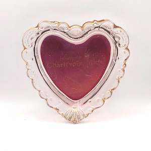 May include: A heart-shaped, clear glass frame with a gold-coloured trim. The frame has a burgundy-coloured interior and the text "Souvenir of Charlevoix, Mich." is visible. The frame is designed with ornate, decorative edges.