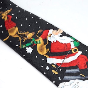 May include: Black Christmas tie featuring Santa Claus skiing and reindeer. Santa is wearing a red suit with a white beard and hat. The reindeer are brown with red and green accents. White snowflakes are scattered across the black background.