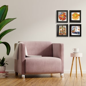 May include: Four framed prints of colorful, intricate artwork depicting ancient Mayan designs and symbols. The prints are arranged in a square formation on a white wall above a pink armchair and a small wooden table.