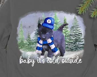 May include: A gray sweatshirt with a black and white puppy wearing a blue hat and scarf. The puppy is standing in a snowy forest scene. The text "baby it's cold outside" is printed below the puppy.