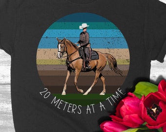 Puede incluir: Una camiseta negra con un gráfico de estilo vintage de una persona montando a caballo. El gráfico está en un círculo con el texto "20 metros a la vez".
