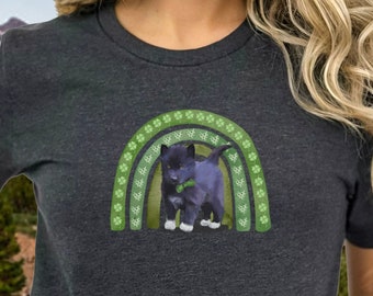 May include: A dark gray short-sleeved t-shirt with a green rainbow and a black kitten wearing a green collar. The text "Bella Canvas 3001" is printed below the image.