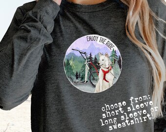 Puede incluir: Una camiseta gris de manga larga Bella Canvas 3501 con un gráfico blanco de un perro tirando de un trineo con el texto "Enjoy the Ride". El texto "choose from: short sleeve, long sleeve or sweatshirt!" también está impreso en la camiseta.