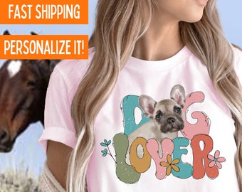 Puede incluir: Camiseta rosa claro con un gráfico colorido de "Dog Lover" que presenta un bulldog francés. El diseño incluye flores y el texto "Dog Lover". La camiseta está hecha de material Bella Canvas de primera calidad.