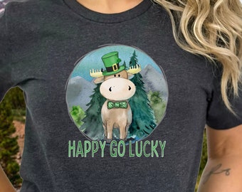 May include: A dark gray short-sleeved t-shirt with a green, white, and brown cartoon moose wearing a green hat with a shamrock. The moose is standing in a green forest with the text "Happy Go Lucky" below it.