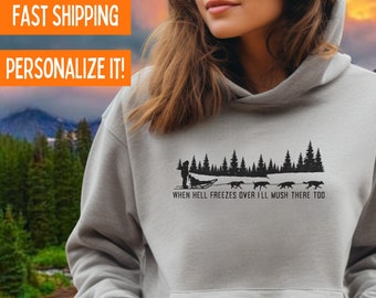 Puede incluir: Una sudadera gris con un gráfico negro de una persona en un trineo tirado por perros con el texto "When hell freezes over I'll mush there too". La sudadera está hecha por Gildan y está disponible en gris deportivo o arena.