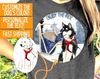 Puede incluir: Una camiseta gris con una ilustración de un perro blanco y negro en un círculo. El texto "Enjoy the Ride" está por encima del perro. El perro lleva un arnés rojo y está tirando de un trineo. La camiseta está disponible en manga corta, manga larga y sudadera.