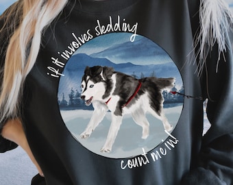 May include: Black sweatshirt with a white circle graphic featuring a husky dog sledding in a snowy mountain landscape. The text "If it involves sledding count me in" is written around the circle.