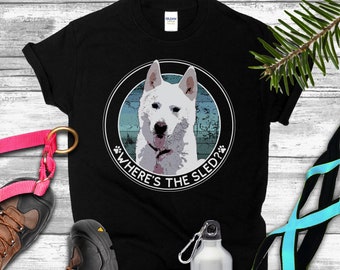 May include: Black t-shirt with a circular graphic featuring a white dog and the text "WHERE'S THE SLED?". The image also includes a pink dog leash, hiking boots, a water bottle, and a black and blue harness.