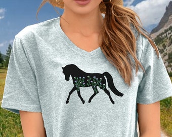 May include: A light blue v-neck t-shirt with a black silhouette of a horse with purple flowers on its body.
