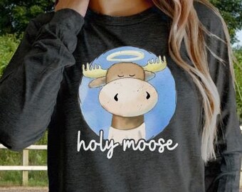 Puede incluir: Una camiseta gris de manga larga con un alce de dibujos animados que lleva un halo. El texto "holy moose" está impreso debajo del alce.
