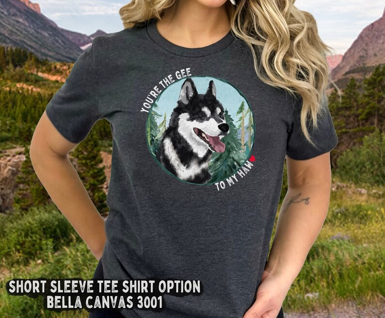 Puede incluir: Una camiseta de manga corta gris oscuro con un gr&aacute;fico de un perro husky blanco y negro en un entorno de bosque. El texto "You're the gee to my haw" est&aacute; impreso en la camiseta.