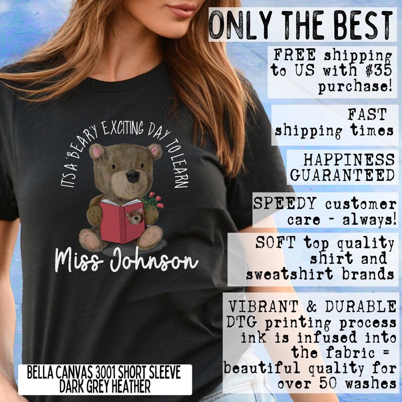 Op de afbeelding: Een zwart T-shirt met een illustratie van een bruine beer die een rood boek vasthoudt. De tekst "It's a Beary Exciting Day to Learn" is in een cirkel rond de beer gedrukt. De tekst "Miss Johnson" is onder de beer gedrukt. Het T-shirt is een Bella Canvas 3001 met korte mouwen in donkergrijs heather.
