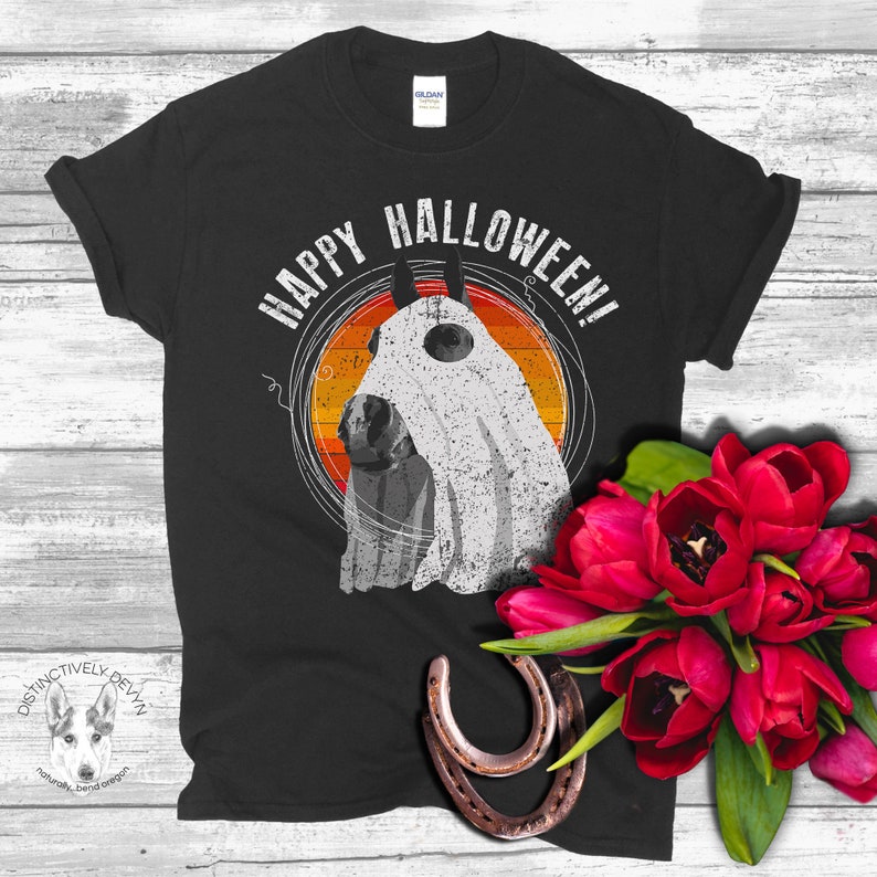 May include: Black t-shirt with a white ghost horse wearing a ghost sheet and the text "Happy Halloween!" printed on it. The shirt is laying on a wooden surface with a bouquet of red tulips and two horseshoes.
