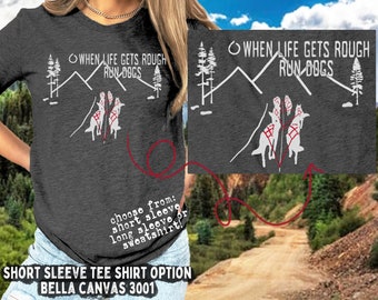 May include: A gray short-sleeved t-shirt with a white graphic of a mountain range and three dogs running. The text "WHEN LIFE GETS ROUGH RUN-DOGS" is printed on the shirt. The shirt is available in short sleeve, long sleeve, or sweatshirt options.