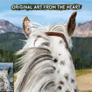 May include: A white horse with brown spots stands in a field with a mountain range in the background. The horse's mane is flowing in the wind. The horse is wearing a brown leather bridle.