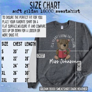 Op de afbeelding: Maattabel voor een donker heather grijs Gildan 18000 sweatshirt. De tabel toont borst- en lengtemaat in inches voor maten S, M, L, XL en 2XL. De afbeelding toont ook een beer die een rood boek draagt en een shirt met de tekst "It's a Beary Exciting Day to Learn" en "Miss Johnson".