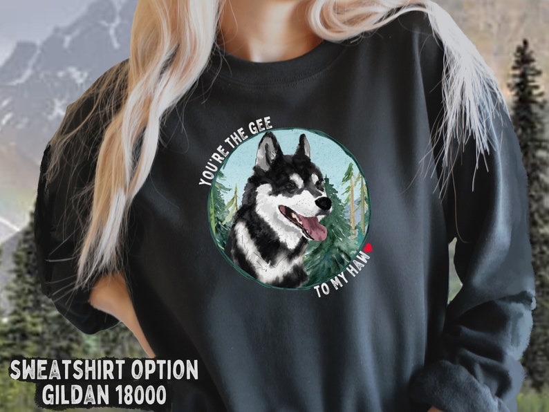 Puede incluir: Sudadera negra con un gr&aacute;fico de un perro husky negro y blanco en una escena de bosque. El texto "You're the Gee to my Haw" est&aacute; impreso alrededor del perro.