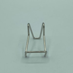May include: A silver metal display stand with a triangular base and two upright supports. The stand is designed to hold small objects, such as figurines or crystals.