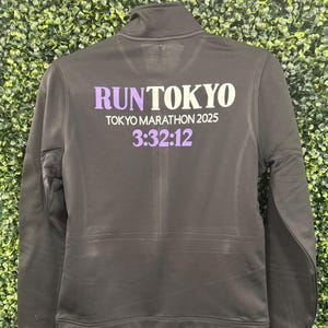 Könnte beinhalten: Schwarze Laufjacke mit "RUN TOKYO" und "TOKYO MARATHON 2025" auf der Rückseite. Die Zeit "3:32:12" ist ebenfalls auf der Rückseite aufgedruckt.